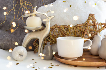 Obraz na płótnie Canvas Cup of coffee tea on Christmas composition with candle, deer, fur pillow, and Xmas baubles on New Year background with bright lights and gold stars. Set of warmth and comfort.