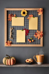 Photo grid board with red and orange paper Autumn leaves and text "Autumn". Fall-related mockup. Orange cup, cookies and decorations on a shelf below the metal grid.