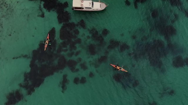 Aerial view travelers on kayak paddling around yacht in crystal lazur sea tith reefs