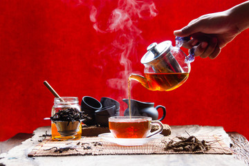 Hands are catching hot tea in the teapot and teacup with steam on reviving the wood and black...