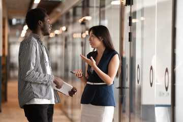 African American businessman and Asian businesswoman talking in hallway