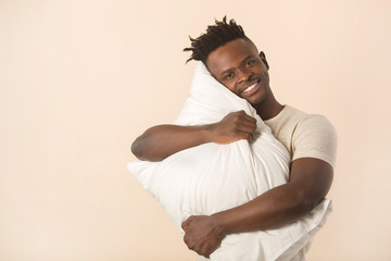 handsome young african man on a beige background with a pillow in his hands