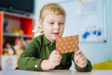 Adorable young girl is looking at a bright card. Preschool concept. Kid's education.