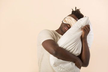 handsome young african man on a beige background with a pillow in his hands