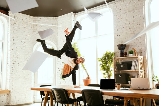 Young caucasian businessman having fun dancing break dance in the modern office at work time with gadgets. Management, freedom, professional occupation, alternative way of working. Loves his job.