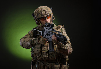 a male soldier in military clothes with a weapon on a dark background