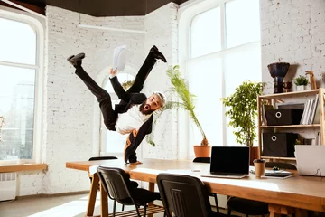 Foto op Plexiglas Young caucasian businessman having fun dancing break dance in the modern office at work time with gadgets. Management, freedom, professional occupation, alternative way of working. Loves his job. © master1305