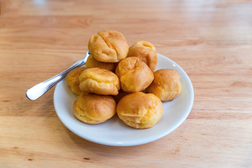 Cream puffs or eclair or choux cream with vanilla custard on wooden table on white plate put on wood table , eat to tea and coffee with cocoa cold, copy space