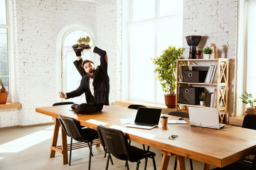 Young caucasian businessman having fun dancing break dance in the modern office at work time with gadgets. Management, freedom, professional occupation, alternative way of working. Loves his job.