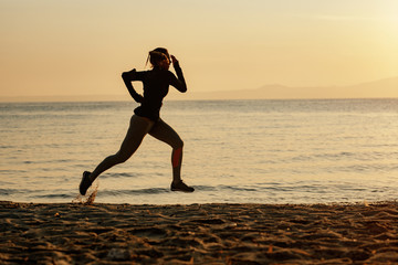 Fototapeta na wymiar Full length of athletic woman running at the beach at sunrise.