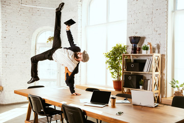 Young caucasian businessman having fun dancing break dance in the modern office at work time with...