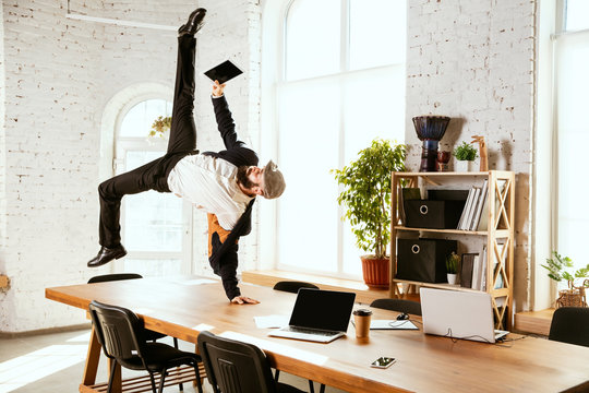 Young caucasian businessman having fun dancing break dance in the modern office at work time with gadgets. Management, freedom, professional occupation, alternative way of working. Loves his job.