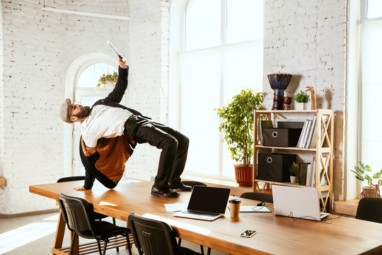 Young caucasian businessman having fun dancing break dance in the modern office at work time with gadgets. Management, freedom, professional occupation, alternative way of working. Loves his job.