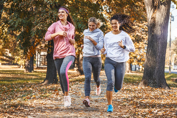 Group of female friends jogging at the city park.Autumn season. - obrazy, fototapety, plakaty