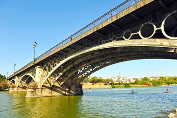 Fototapeta premium Canoeists sailing under the Triana Bridge on the Guadalquivir River in Seville Spain