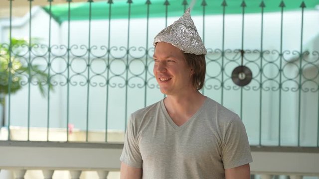 Happy young man wearing tin foil hat and thinking outdoors