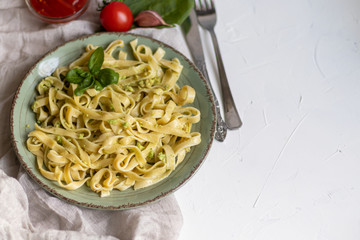 Italian pasta, spaghetti with avocado, spinach, basil, cream, cheese. Vegetarian vegetable pasta. Spinach with noodles. On a light background. Nearby are cherry tomatoes, olive oil. Copy space. 