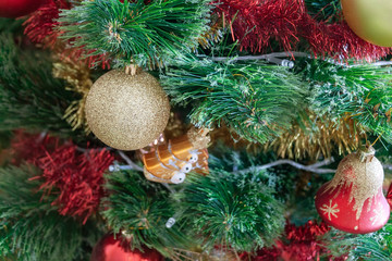 Green artificial Christmas tree decorated with beautiful golden sparking ball, red and gold garlands, and other toys. Selective focus