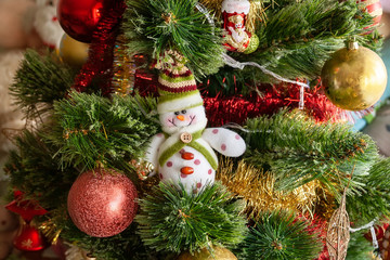 Green artificial Christmas tree decorated with beautiful smiling textile snowman, red and golden garlands and other toys. Home decoration for a family holiday