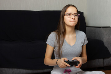 Young european dark-haired teen girl plays video games at home. Real emotions, excitement