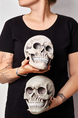 Tattooed hands of a woman in a black watch and clothes are holding a realistic model of a human skulls with teeth isolated on white. Close-up shot.