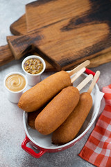 Corn dogs with mustard, elevated view over beige stone surface with rustic wooden chopping boards in the background