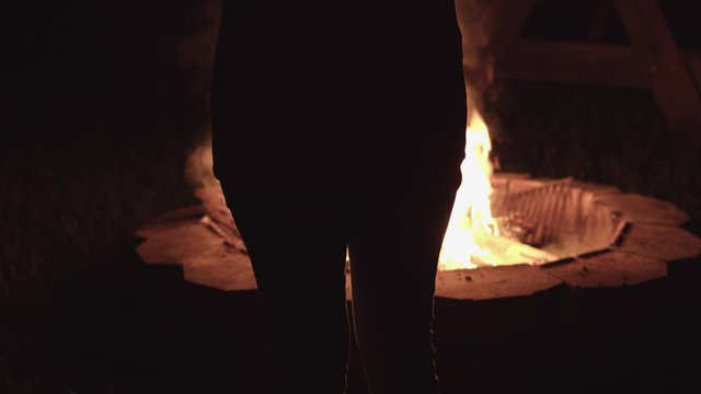 A woman stands by a fire pit.