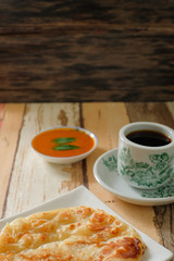 A cup of hot coffee , Roti canai or Roti Parata , dalca and curry sauce on wood background