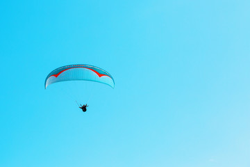Paraglider soars against the blue sky with clear space.