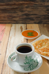 A cup of hot coffee , Roti canai or Roti Parata , dalca and curry sauce on wood background