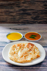 A cup of hot coffee , Roti canai or Roti Parata , dalca and curry sauce on wood background