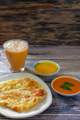 A cup of hot coffee , Roti canai or Roti Parata , dalca and curry sauce on wood background