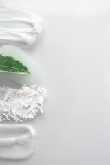 Fresh green leaf and smear moisturizer and translucent loose powder on white background. Natural skin care concept, top view