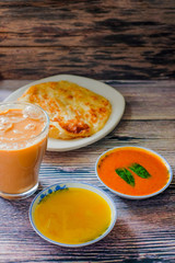 A cup of hot coffee , Roti canai or Roti Parata , dalca and curry sauce on wood background