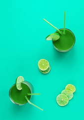 Healthy green smoothie in two glasses with cocktail straws garnished with lime. Flat lay background. Food and drink, dieting and nutrition concept.