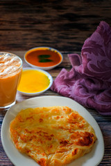 A cup of hot coffee , Roti canai or Roti Parata , dalca and curry sauce on wood background