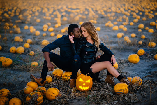 Couple sitting in field near scary face pumpkin, concept halloween - Powered by Adobe