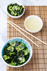 Traditional Japanese dish tasty appetizing seaweed salad served with cucumber in white bowl top view.Organic natural product.Raw,vegan,vegetarian foodVertical orientation