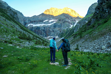 Fototapeta na wymiar A couple standing on a meadow with the view on Schladming Alps, partially still covered with snow. Spring slowly reaching the tallest parts of the mountains. Soft sunrise on the mountain peaks.