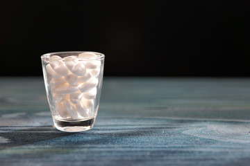 White pills in a glass on wooded table.