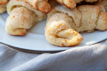 Closeup view of ruddy sugar-frosted croissants from a curd dough lying on a white plate next to a gray cloth. Sweet baked bagels just taken out of the oven. A delicious tea snack for breakfast