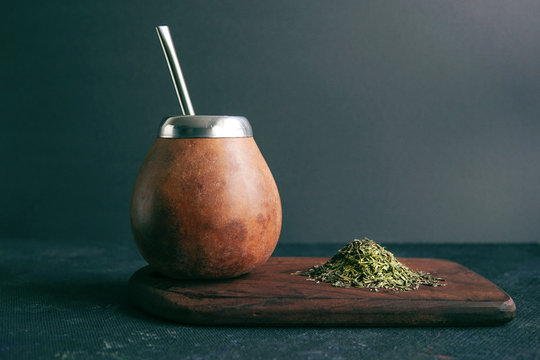 Calabas and a bombilla with a bunch of mate tea on a wooden plate on dark background. Organic traditional tea. Free space for your text.