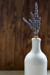 White glass bottle with lavender flowers on wooden background. Selective focus.