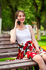 Calling by phone. Beautiful girl in summer dress sitting on a park bench