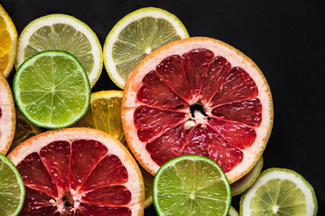 Slices of pink Star Ruby grapefruit and green lime on black background