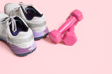 Sneakers and pink dumbbells fitness, isolated on pink surface.