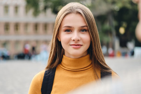Portrait of beautiful smiling casual student girl dreamily looking in camera on street