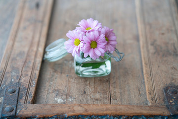 Purple flowers in a glass on a used shabby wooden interior 