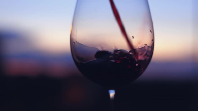Pouring red wine into a glass at sunset, slow motion