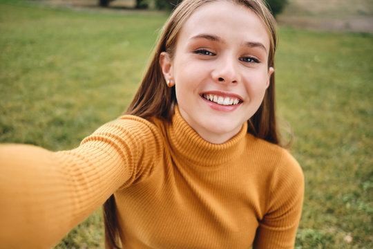 Portrait of attractive smiling casual girl joyfully taking selfie in city park